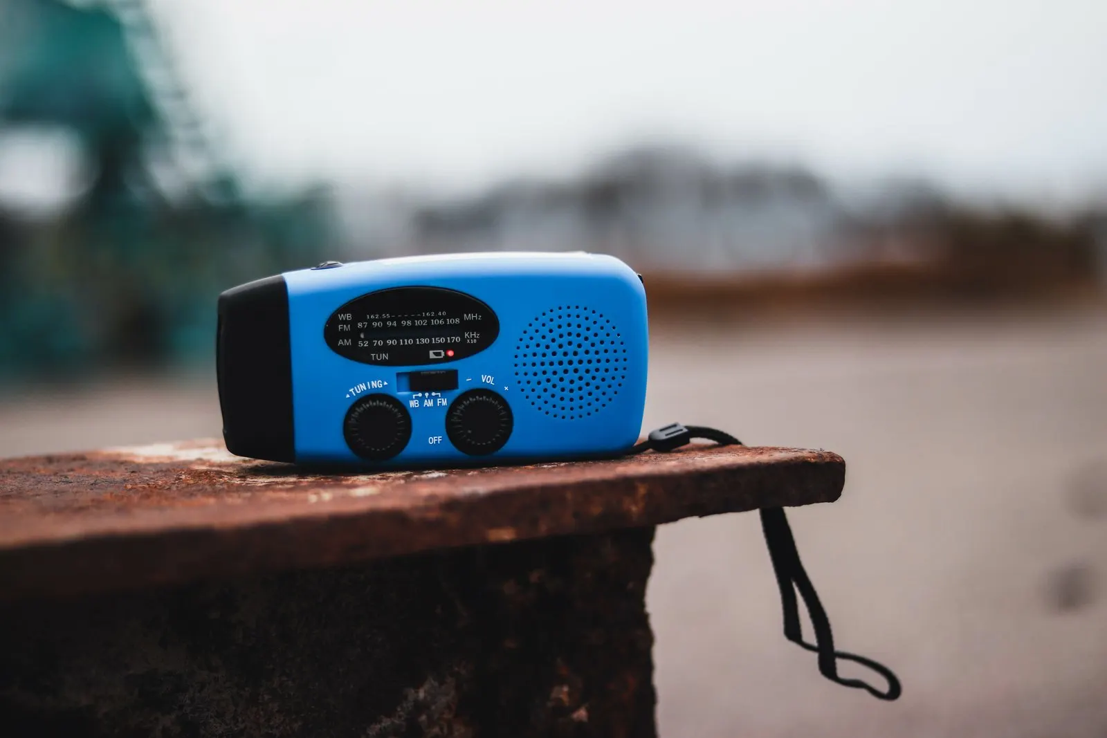 NOAA weather radio guide: a blue portable weather-band radio on a rusty metal ledge